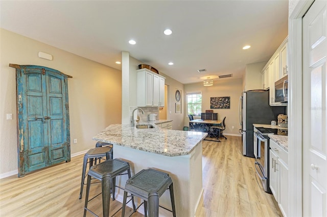 kitchen with light stone countertops, white cabinetry, sink, light hardwood / wood-style floors, and appliances with stainless steel finishes