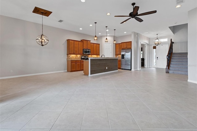 kitchen featuring ceiling fan with notable chandelier, appliances with stainless steel finishes, hanging light fixtures, a kitchen island with sink, and light tile patterned flooring