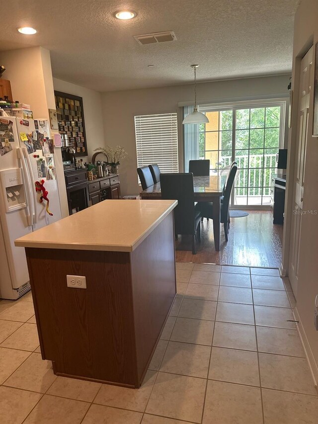 kitchen featuring white fridge with ice dispenser, a textured ceiling, light hardwood / wood-style flooring, decorative light fixtures, and a kitchen island