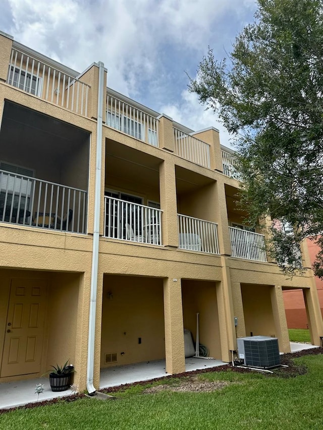 exterior space featuring central AC unit, a lawn, a patio, and a balcony