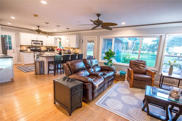 living room featuring ceiling fan, ornamental molding, and light hardwood / wood-style flooring