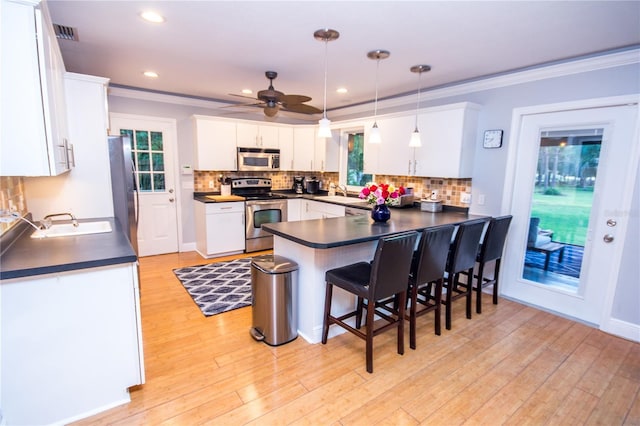 kitchen with kitchen peninsula, stainless steel appliances, white cabinetry, and hanging light fixtures