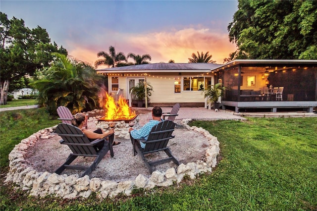 back house at dusk featuring a patio area, a yard, and a fire pit