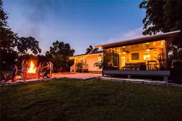 yard at dusk featuring a fire pit, ceiling fan, and a deck