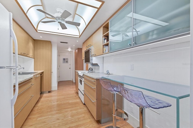 kitchen with sink, light stone counters, ceiling fan, white appliances, and light hardwood / wood-style floors