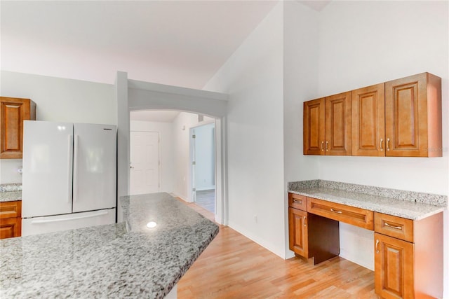 kitchen featuring light stone countertops, vaulted ceiling, built in desk, light hardwood / wood-style flooring, and white fridge