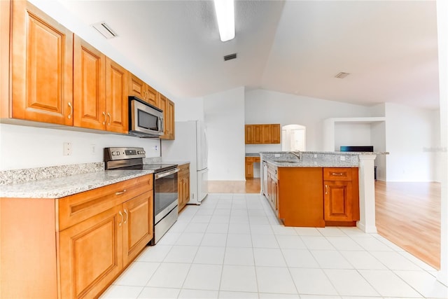 kitchen with sink, light stone counters, vaulted ceiling, light tile patterned floors, and appliances with stainless steel finishes