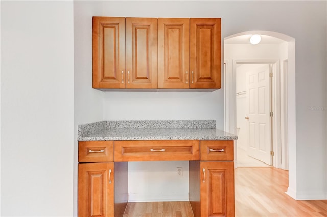 kitchen featuring built in desk, light hardwood / wood-style floors, and light stone counters