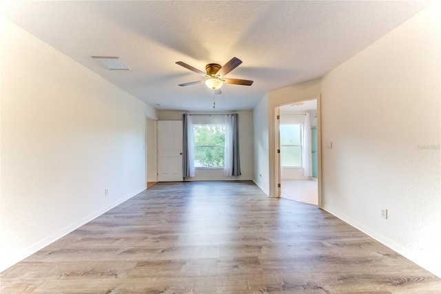 empty room with ceiling fan, light wood-type flooring, and a textured ceiling