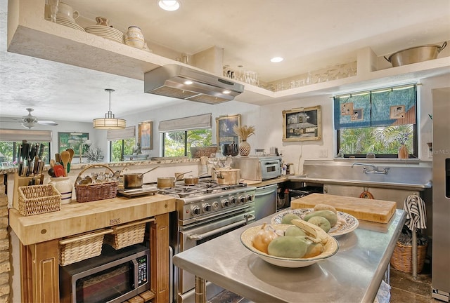 kitchen featuring ventilation hood, ceiling fan, decorative light fixtures, stainless steel appliances, and stainless steel counters