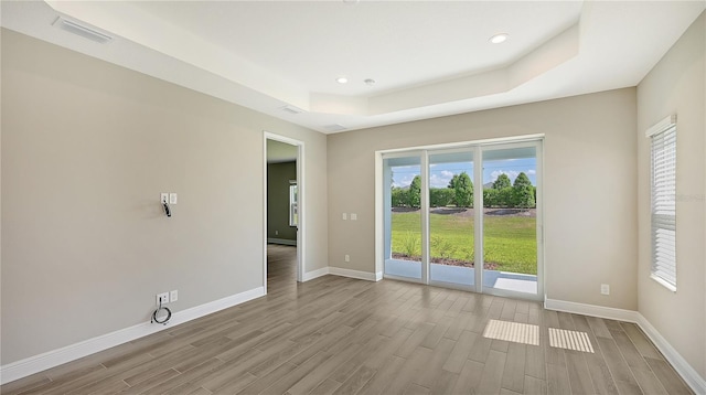 spare room with a raised ceiling and light hardwood / wood-style floors