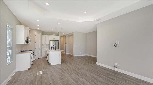 kitchen featuring a center island with sink, stainless steel appliances, light hardwood / wood-style floors, a tray ceiling, and white cabinets