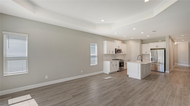 kitchen featuring appliances with stainless steel finishes, a kitchen island with sink, white cabinets, and a raised ceiling