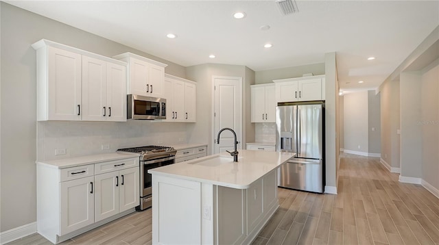 kitchen with appliances with stainless steel finishes, sink, an island with sink, and white cabinets