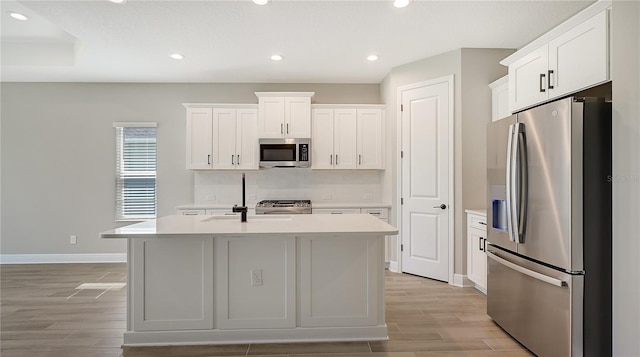 kitchen featuring a center island with sink, appliances with stainless steel finishes, white cabinets, and tasteful backsplash