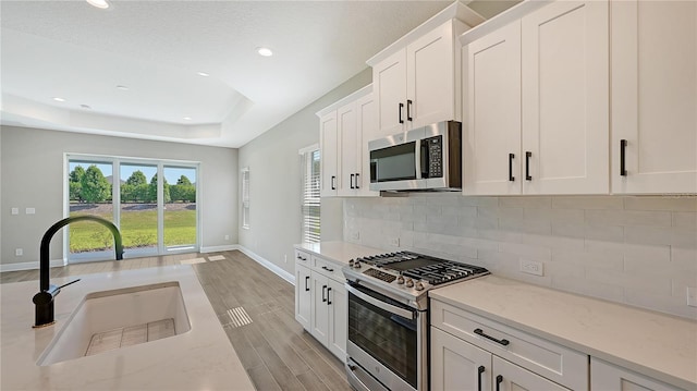 kitchen featuring appliances with stainless steel finishes, white cabinetry, light stone countertops, and sink