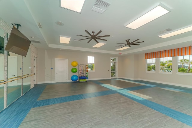 exercise area with hardwood / wood-style floors, ceiling fan, and a raised ceiling