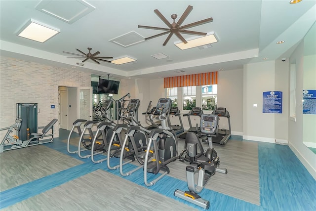 gym featuring a raised ceiling, hardwood / wood-style flooring, ceiling fan, and brick wall