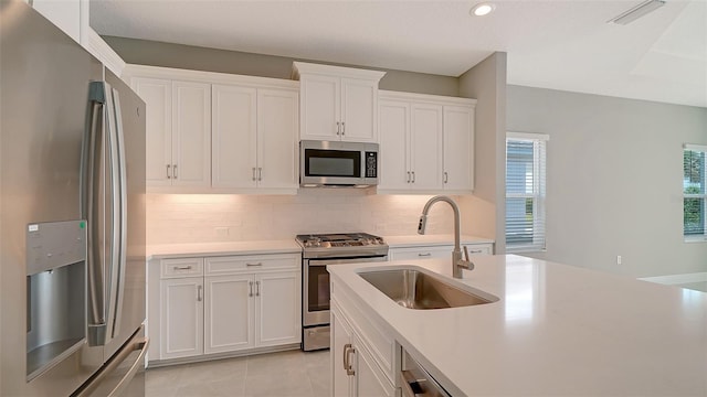 kitchen with appliances with stainless steel finishes, white cabinets, backsplash, light tile patterned floors, and sink