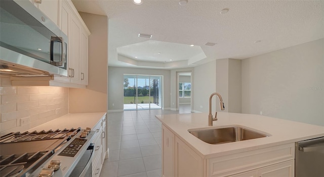 kitchen featuring a raised ceiling, backsplash, sink, white cabinetry, and appliances with stainless steel finishes