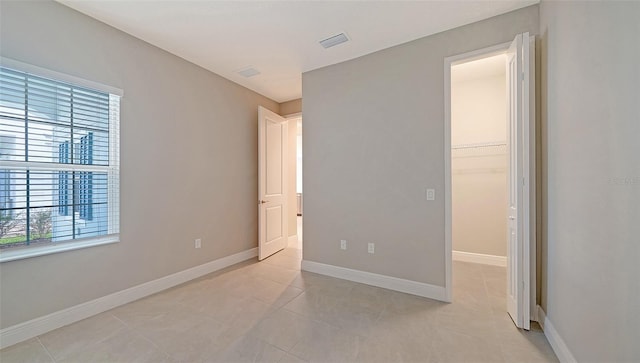 unfurnished bedroom with multiple windows, a walk in closet, and light tile floors