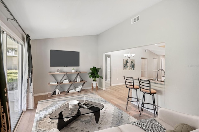 living room with a notable chandelier, sink, vaulted ceiling, and light wood-type flooring