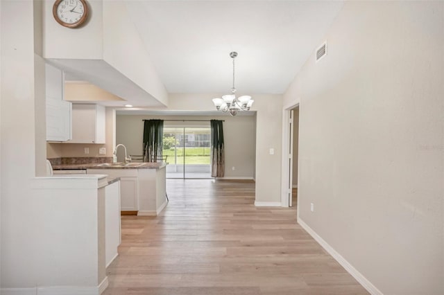 kitchen with white cabinetry, a notable chandelier, decorative light fixtures, lofted ceiling, and light wood-type flooring