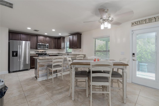 kitchen featuring ceiling fan, light tile patterned floors, dark brown cabinetry, light stone countertops, and appliances with stainless steel finishes