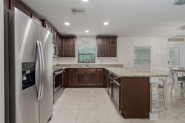 kitchen featuring stainless steel appliances, sink, light stone counters, a kitchen bar, and kitchen peninsula