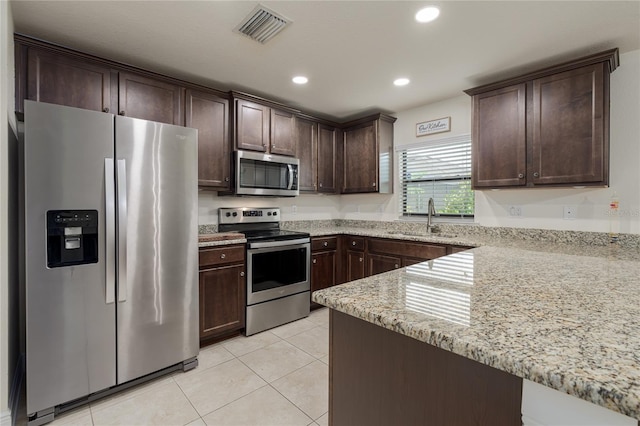 kitchen with stainless steel appliances, sink, light stone countertops, and dark brown cabinetry