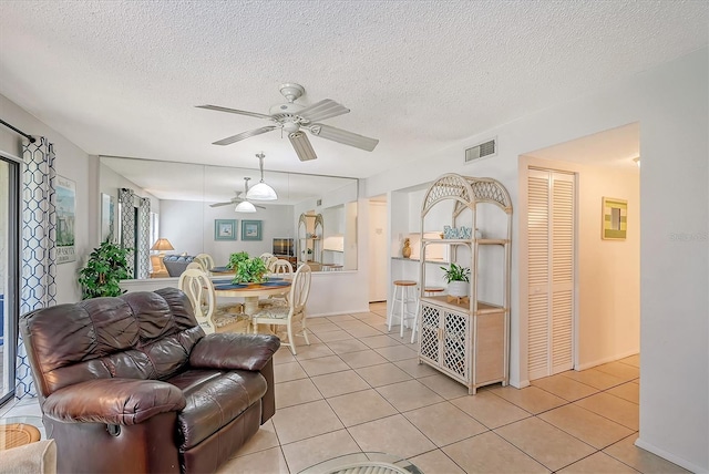 living room with a textured ceiling, ceiling fan, and light tile patterned floors