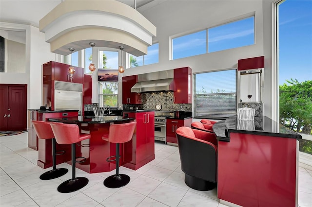 kitchen featuring premium appliances, light tile patterned floors, tasteful backsplash, and wall chimney range hood