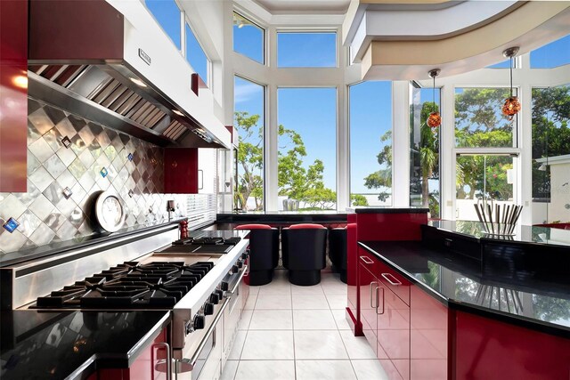 kitchen with light tile patterned floors, backsplash, high end stainless steel range oven, hanging light fixtures, and wall chimney exhaust hood