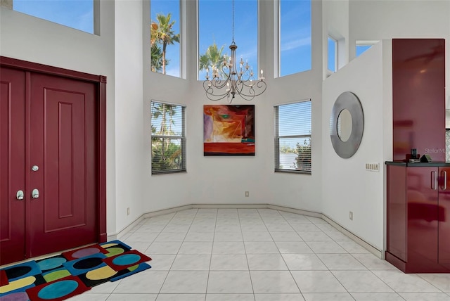 foyer entrance with a notable chandelier, light tile patterned flooring, a wealth of natural light, and a high ceiling