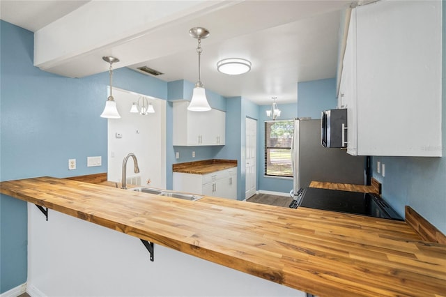 kitchen with wood counters, sink, kitchen peninsula, decorative light fixtures, and white cabinetry