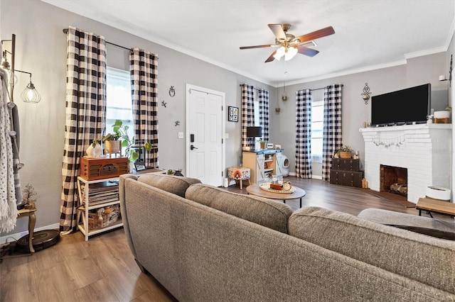 living room featuring hardwood / wood-style floors, ceiling fan, crown molding, and a brick fireplace