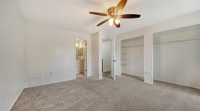 unfurnished bedroom featuring two closets, light carpet, connected bathroom, and ceiling fan