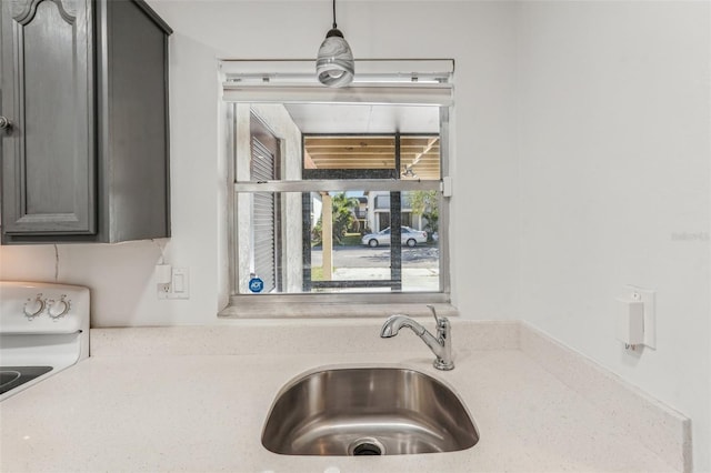 kitchen with light stone countertops, sink, pendant lighting, and range