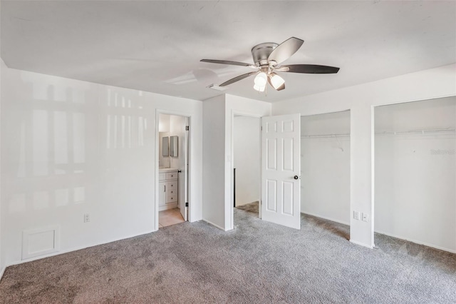 unfurnished bedroom featuring ceiling fan, two closets, light colored carpet, and ensuite bath