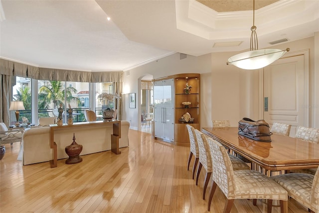 dining space featuring a raised ceiling, crown molding, and light hardwood / wood-style flooring