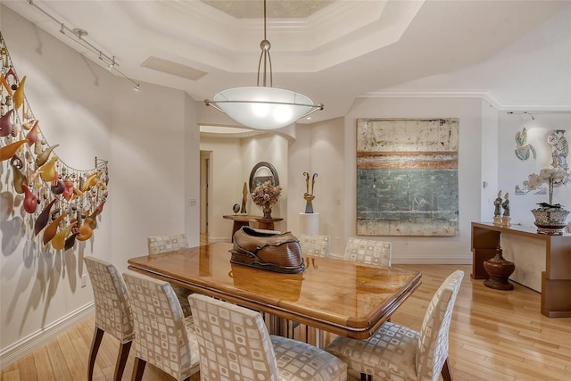 dining room featuring crown molding, a raised ceiling, and light wood-type flooring