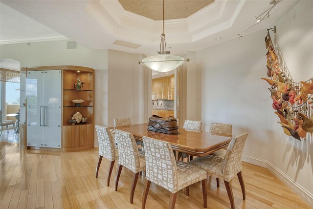 dining space with light hardwood / wood-style flooring, a raised ceiling, and ornamental molding