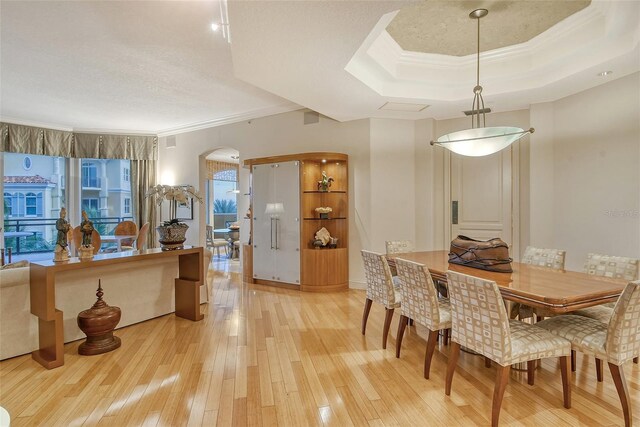 dining space with light hardwood / wood-style flooring, ornamental molding, and a tray ceiling