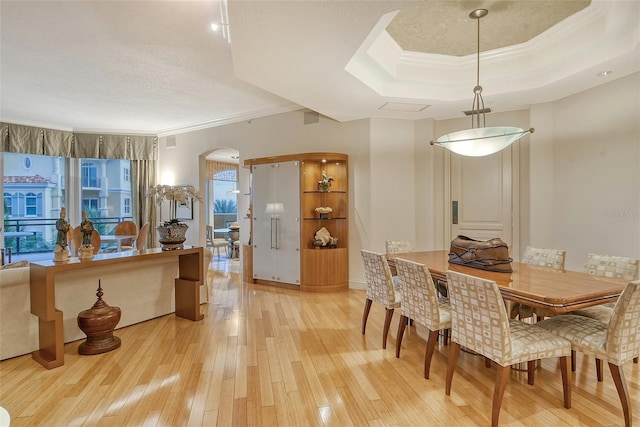 dining space with crown molding, a tray ceiling, a textured ceiling, and light hardwood / wood-style flooring