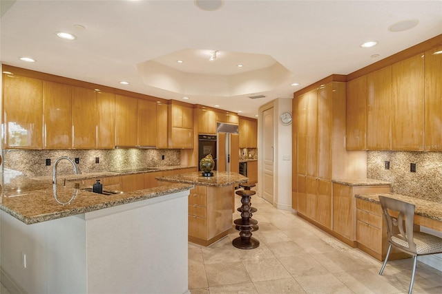 kitchen with a center island, kitchen peninsula, a raised ceiling, light stone countertops, and black appliances