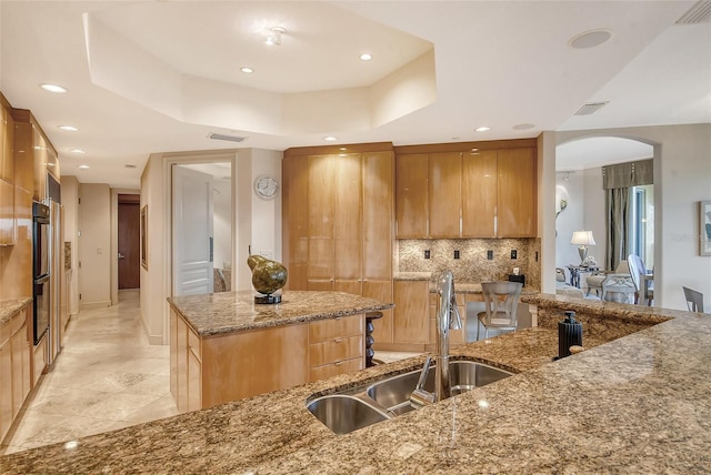 kitchen with decorative backsplash, stone countertops, a tray ceiling, light tile patterned floors, and sink