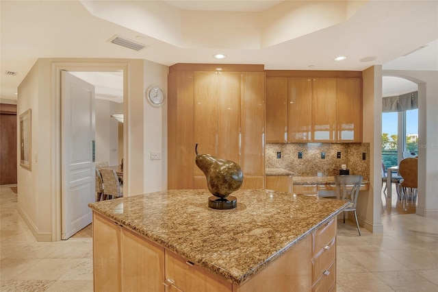 kitchen with tasteful backsplash, light tile patterned floors, a center island, and light stone countertops