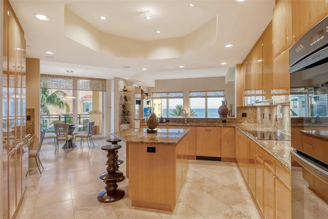 kitchen with a center island, light stone counters, a tray ceiling, black electric cooktop, and kitchen peninsula