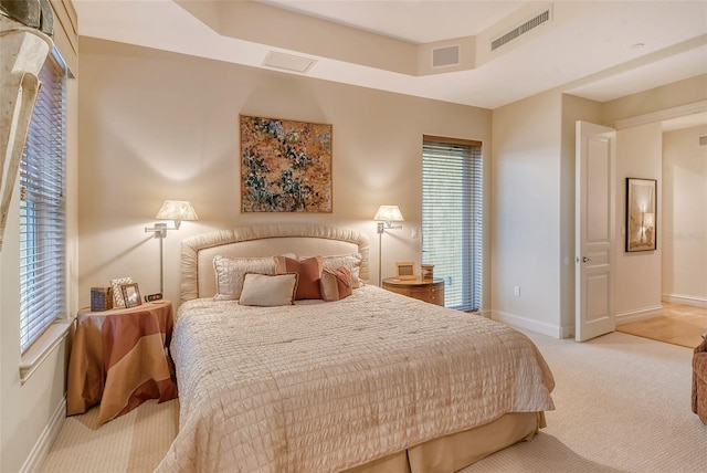 bedroom with a tray ceiling, light colored carpet, and multiple windows