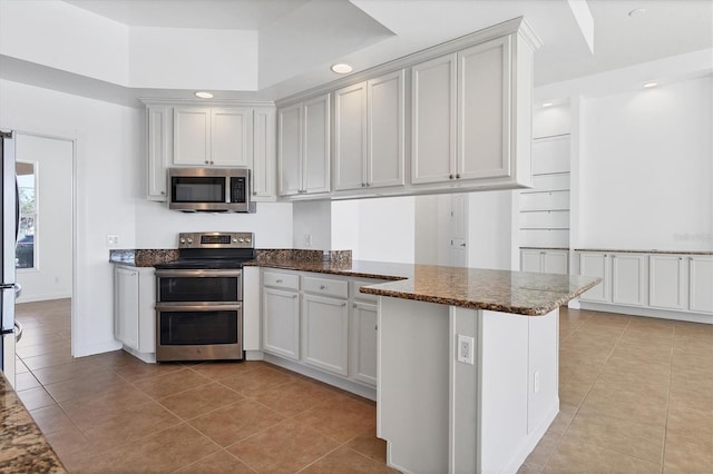 kitchen featuring kitchen peninsula, stainless steel appliances, light tile patterned floors, dark stone countertops, and white cabinetry